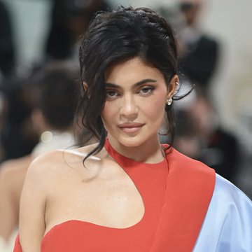 A woman with dark hair pulled back poses at an event in a red and white asymmetrical dress. The image appears to feature Kylie Jenner, whose X account promotion of the $KYLIE memecoin is the subject of the accompanying post discussing alleged coordinated wallet extraction of 2,425 SOL by insiders.