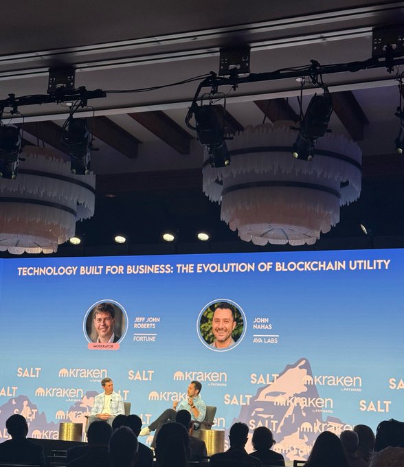 A conference stage at a Kraken and SALT event titled 'TECHNOLOGY BUILT FOR BUSINESS: THE EVOLUTION OF BLOCKCHAIN UTILITY' features moderator Jeff John Roberts of Fortune speaking with John Nahas of Ava Labs, under ornate chandeliers.