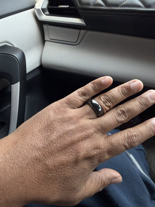 A hand wearing a sleek black Tangem ring sits on a car dashboard, showcasing the wearable crypto wallet as a stylish accessory. The image reinforces the post's message about recommending Tangem to trusted people for secure self-custody, with the ring serving as a fashionable entry point into crypto ownership.