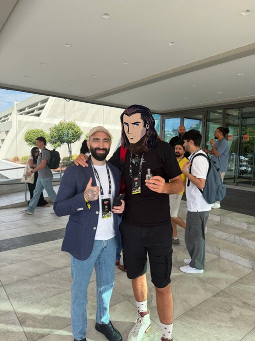 A man in a blazer and beanie poses with someone wearing an oversized cartoonish mask at what appears to be a crypto/NFT event, both wearing event lanyards. The caption suggests they're with a notable figure (@mert) from the Quant community, who shares their love for the MadLads NFT PFP aesthetic — humorously echoed by the mask that looks like a stylized cartoon portrait, matching the MadLads style.
