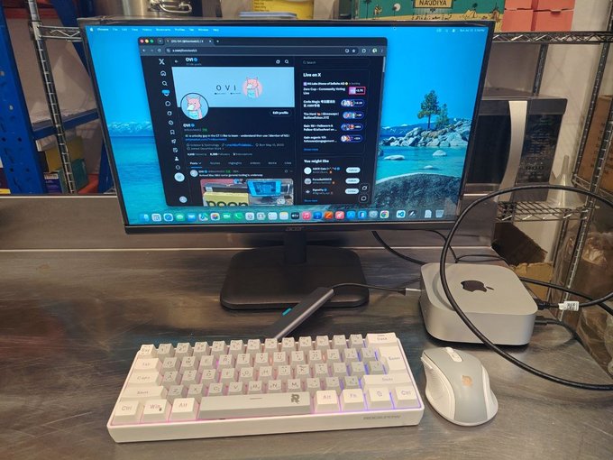 A sleek Mac mini sits on a desk next to a monitor displaying Twitter/X, a white mechanical keyboard, and a gaming mouse, celebrating @0xoviweb3's new setup as a reward for his dedication and consistency in the crypto/web3 space.