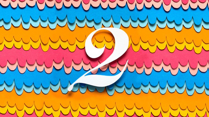 A large white stylized number '2' on a colorful background of layered scalloped patterns in orange, blue, pink, and yellow.