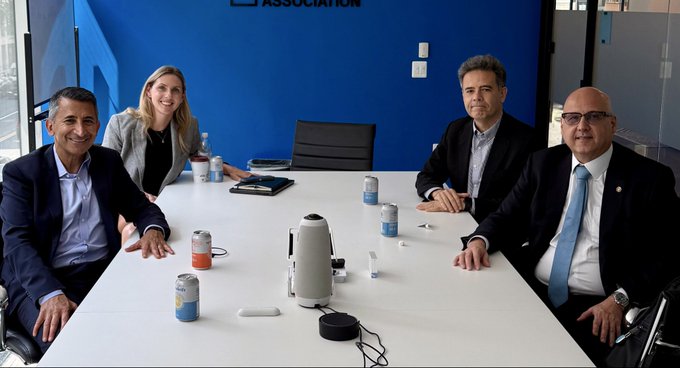 Four professionals sit around a conference table in a meeting room with a blue wall displaying partial "ASSOCIATION" text, alongside beverage cans and a small speaker device on the table. The image captures a formal business meeting between Coinbase representatives and CVM (Brazilian Securities Commission) President Otto Lobo, reflecting the post's discussion about Brazil's role in tokenized capital markets and Coinbase's Latin American hub strategy.