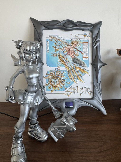 A silver chrome Sailor Moon figurine stands next to an ornate silver-framed digital display showing Sailor Moon artwork with the word 'SINGER' visible.