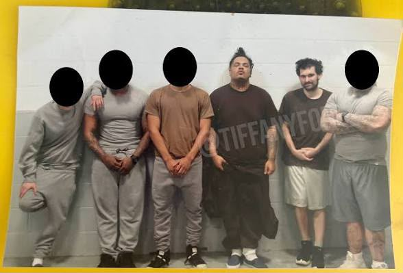 Mugshot-style photo of six men lined up against a wall with faces blurred, one wearing an 'TIFFANY FOR...' shirt, set on a yellow background.