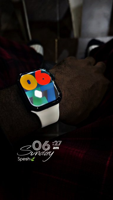 A close-up of an Apple Watch on a person's wrist displaying a colorful watch face, with overlay text reading '06:27 am', 'Sunday', and 'Spesh'.