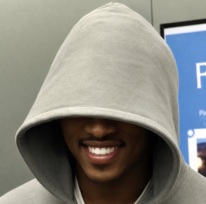 A close-up photo of a smiling man wearing a gray hoodie that obscures his eyes.
