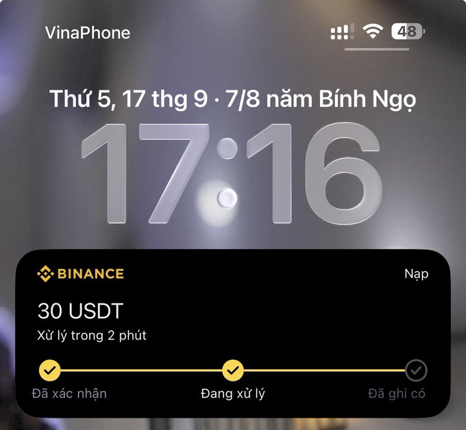 An iPhone lock screen shows the time 17:16 on VinaPhone, with a Binance notification indicating a 30 USDT deposit being processed ("Đang xử lý").