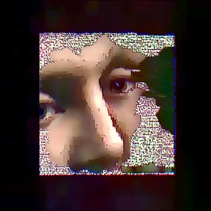 A distorted, glitchy image showing a face with hands near it, surrounded by static interference patterns on a screen.