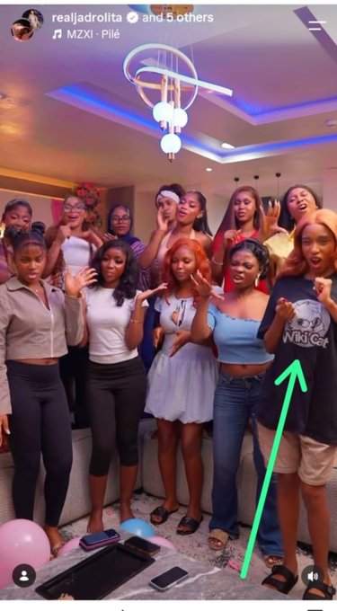 A group of young women are posing for a photo, with one woman on the right wearing a t-shirt that says "Wiki Cat". This relates to the post by mentioning the stock ticker "$WKC" and implying this woman's shirt is a clever reference to it.