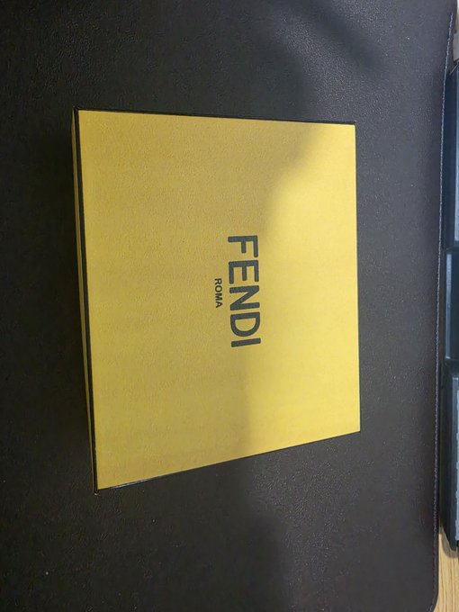 A yellow Fendi Roma box with the brand name in blue lettering rests on a dark surface.