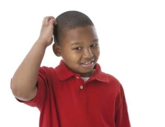 A young boy in a red polo shirt is smiling and scratching the back of his head against a white background.