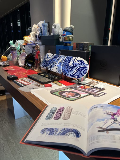 A display table featuring various designer toys and figurines, including Gundam-style models, alongside open art books showcasing skateboard deck graphics.