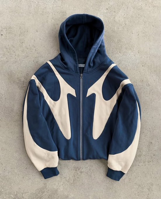 A navy blue and cream zip-up hoodie with a Nike logo, featuring a bold abstract graphic design, laid flat on a concrete surface.