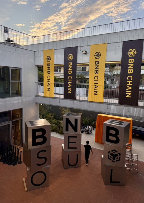 A sneak peek of the #BNBSeoul setup reveals large block letters spelling "BSO," "NEU," and "BNB" arranged in a courtyard, with multiple "BNB CHAIN" banners hanging from the upper level. The arrangement of letters and branding directly previews the upcoming BNB Seoul event.