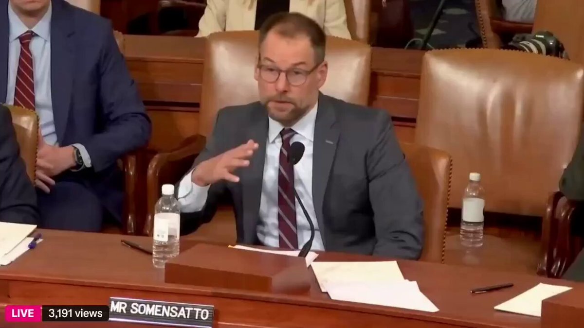 The image shows a man sitting at a wooden desk, wearing glasses and a suit, with his hand raised as if he's speaking or gesturing during a meeting. The scene takes place inside a room where several people are seated around a table, including a man in a suit who appears to be the center of attention.

The image also contains text that reads "Coin Center Director of Policy Jason Somensato says Bitcoin should be given a de minimis tax exemption This means Bitcoin could fall under a tax-free bracket". The post suggests that Bitcoin might be subject to a tax break, which is relevant to the man's position at the table.