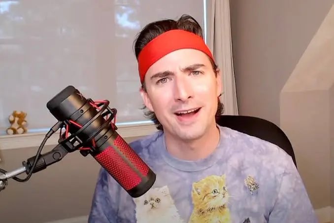 Roaring Kitty (Keith Gill), known for his role in the GameStop short squeeze, is shown in his signature red headband and cat-printed sweatshirt, speaking into a microphone—a fitting image for the post celebrating a new meme coin tied to GameStop ($GME) and saying "I like the stock."