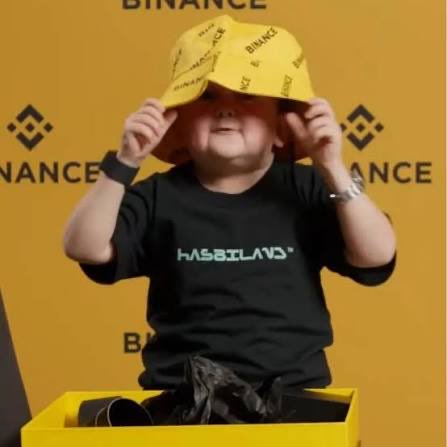 A person wears a yellow Binance-branded bucket hat and a black "HASBILAND" t-shirt while pulling the hat down over their eyes, set against a yellow Binance backdrop. The meme visually echoes the post's theme of defending Binance and its founder CZ from coordinated smear campaigns by centralized exchanges and VC firms, with the hat symbolically shielding its identity from critics.