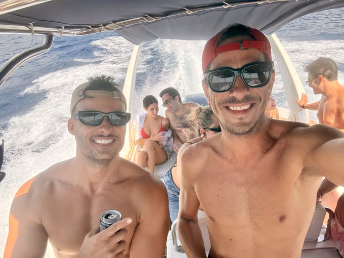 Two young men beam from the deck of a boat under the text "Before I formed you in the womb I knew you" (Jeremiah 1:5), seemingly spoofing the reality-TV dating show "The Bachelor" by joking that "crypto bachelor" is the next frontier—and one is holding a can as if toasting to Carlos getting in "pre-bond" on the launch.