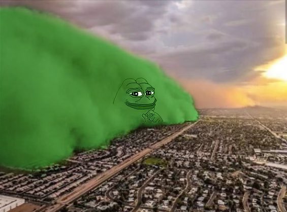 An aerial view of a sprawling suburban landscape under a cloudy sunset sky, with a massive wave of bright green smoke rolling across the cityscape, featuring a Pepe the Frog meme face digitally overlaid in the center of the smoke cloud.