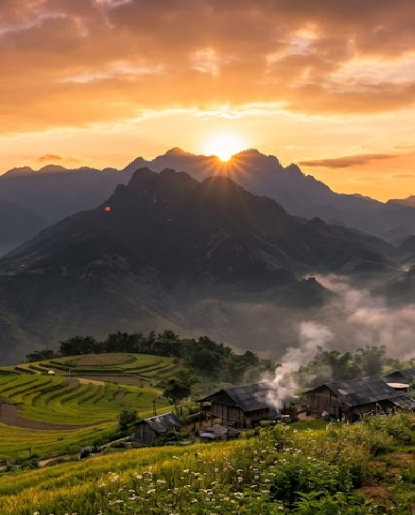 A scenic landscape photograph showing a sunset over mountains with a village in the valley below, featuring terraced rice fields and traditional houses with smoke rising.
