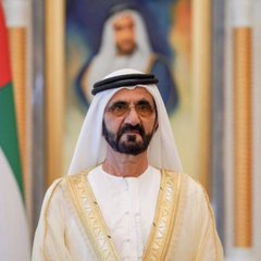 A portrait of Sheikh Mohammed bin Rashid Al Maktoum, the ruler of Dubai, wearing traditional Emirati attire in front of a UAE flag and a portrait of Sheikh Zayed.