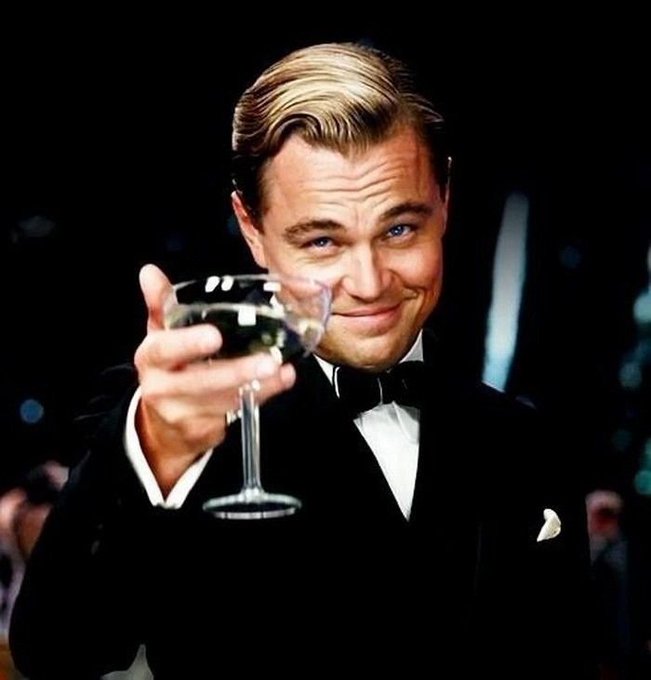 A famous image of Leonardo DiCaprio in a black tuxedo, smiling and toasting with a coupe glass of champagne in front of a dark background.