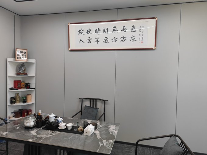A tea room with gray walls features a Chinese calligraphy scroll reading '色即是空空即是色 受想行识亦复如是 入甚深法界得無所得 大自在矣', alongside a marble tea table set and a shelf displaying teaware.