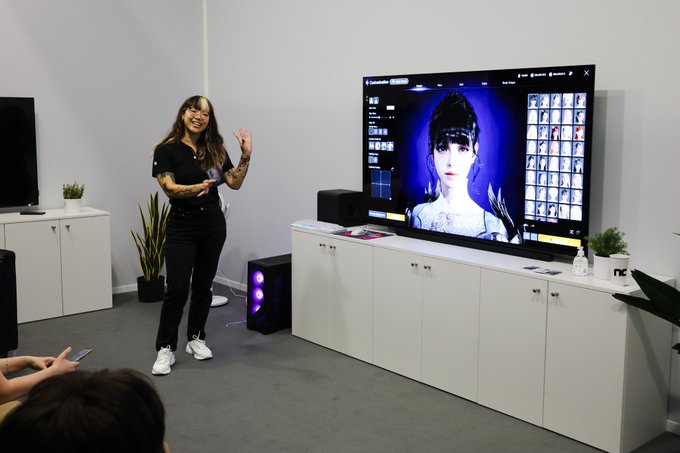 A woman presents at a B2B booth, showcasing the AION 2 video game on a large display screen, with an audience seated nearby.
