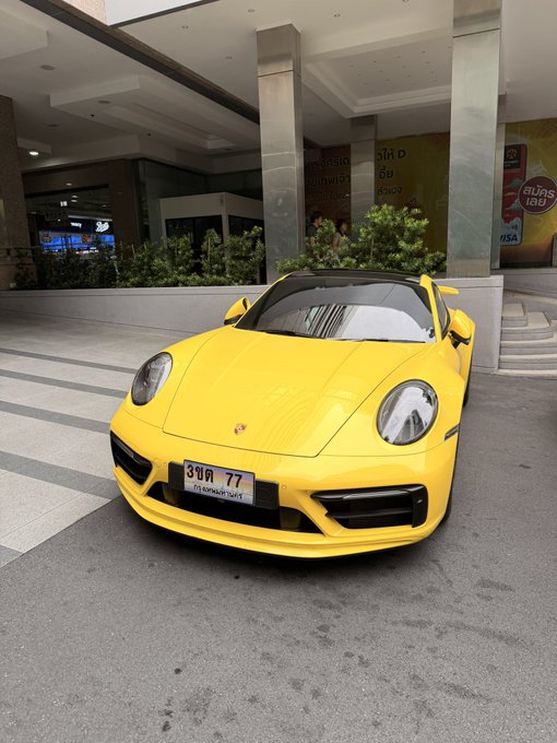 A bright yellow Porsche 911 with Thai license plate '3ขค 77' is parked in front of a building with Burgrill 180 signage.