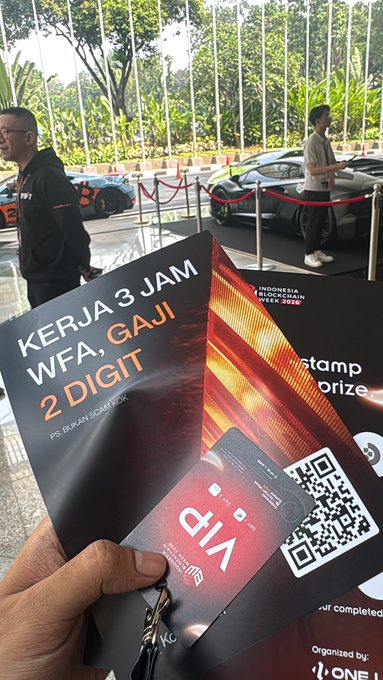 A hand holds a promotional flyer reading "KERJA 3 JAM WFA, GAJI 2 DIGIT" with a VIP QR code, while in the background a "Stamp Your Prize" event sign and several luxury cars are visible at what appears to be an Indonesia BlockChain Week 2026 event, fitting a "gm" (good morning) crypto greeting.
