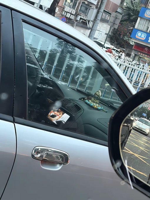 A silver car window reveals a dashboard adorned with a beaded ornament and what appears to be a "freedom of money" charm, fitting the post's cynical commentary on insider trading—where those with inside information profit handsomely while retail investors lose everything.