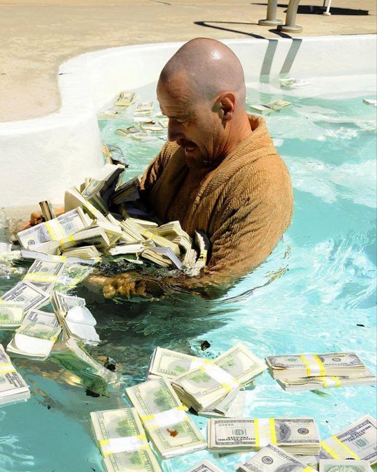 A bald man in a brown bathrobe stands in a swimming pool completely surrounded by stacks of banded US currency, holding a ledger book.