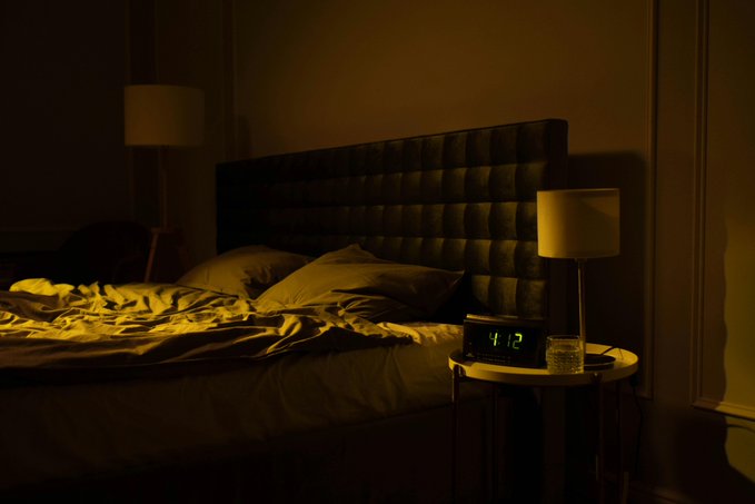 The image shows a bedroom with a bed covered in white sheets and two lamps, one of which has a green light. The room appears dark, creating an atmosphere of relaxation or rest. There are also some objects placed around the room, such as a clock on a table near the bed and another lamp further away from the bed. The image seems to be related to a post about AI projects that focus on Web3, Quantum, and ARCTERMINALs.