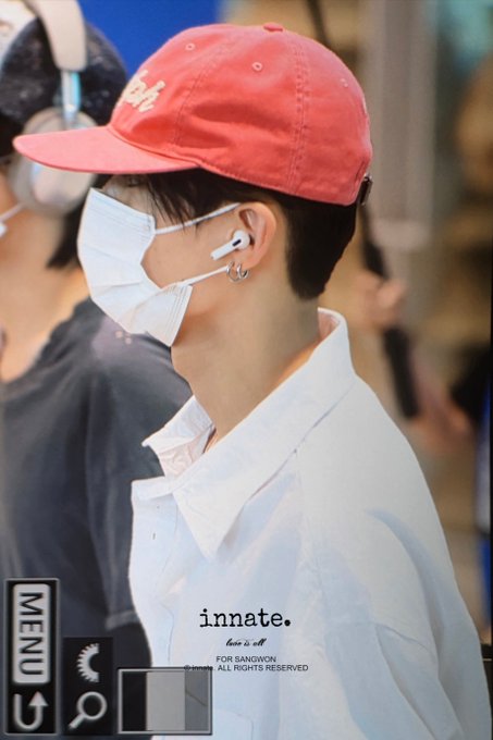 A person in profile wearing a red cap, white face mask, white shirt, and AirPods, with 'innate' text and a MENU button overlay visible.