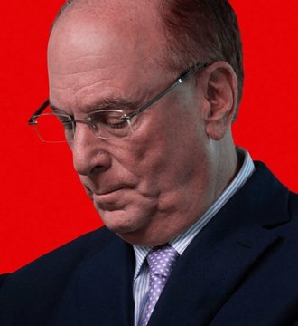 A close-up portrait of a bald older man wearing glasses, a dark suit, and a purple patterned tie, photographed against a bright red background.