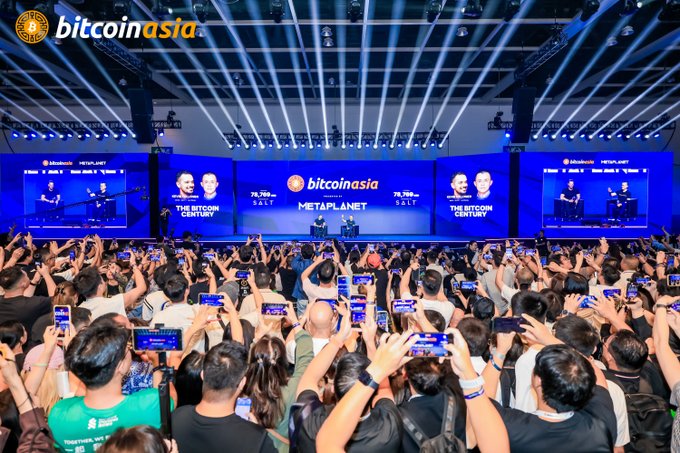 A packed conference hall at Bitcoin Asia 2026 features a stage with speakers addressing an enthusiastic crowd, all holding up their phones under blue spotlights. The screens prominently display "bitcoin asia," "METAPLANET," and the slogan "THE BITCOIN CENTURY" alongside a Bitcoin price ticker showing "78,769" SALT, capturing the bullish energy celebrated in the post.