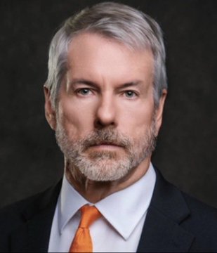 A formal portrait of a middle-aged man with gray hair and a beard, wearing a dark suit, white shirt, and orange tie against a dark background.