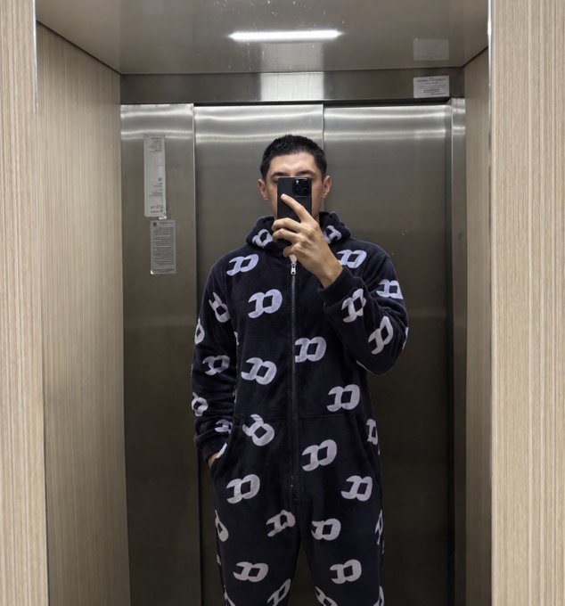 A person taking a mirror selfie in an elevator wearing a dark blue onesie covered in a repeating white 'D' pattern.
