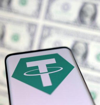 The Tether (USDT) logo is displayed on a smartphone screen against a backdrop of blurred U.S. dollar bills, symbolizing the cryptocurrency's tie to traditional currency. This visual aligns with the news of two Thai businessmen suing Tether for allegedly freezing $42.4 million in USDT at the request of U.S. authorities.
