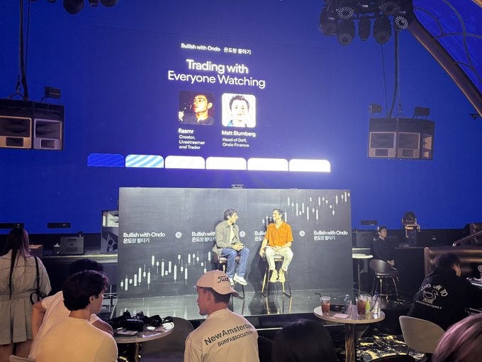 A photo from a 'Bullish with Ondo' panel discussion titled 'Trading with Everyone Watching,' featuring speakers Rasmus (Livestreamer and Trader) and Matt Bumberger (Head of Ondo Finance) on stage.