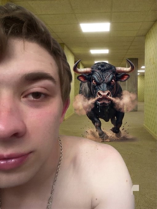 A selfie of a shirtless young man with a chain necklace in a yellow hallway, with an angry charging bull digitally added behind him.