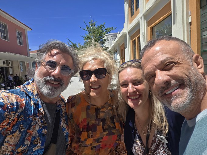 The image features a group of four people posing for a photo together outside. They are all smiling and appear to be enjoying each other's company, possibly reminiscing about old memories or making new ones. The background includes buildings and trees, suggesting that they might be in an urban setting with some greenery around them. The post caption reads: "This space is all about catching up with old friends and making new ones, and @NFCsummit does it better than anyone! So good to hang out with the wonderful @FamilyDogecoin and @Tulipaniart again, and to finally meet the legend @AdamWeitsman. Good times!". Focus on what is in the image and how it relates to the post.