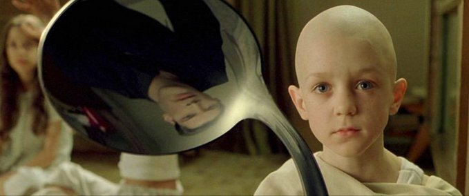 A bald young girl with pale skin and intense blue eyes holds a large silver ladle in front of her, with a reflection visible in the polished surface.