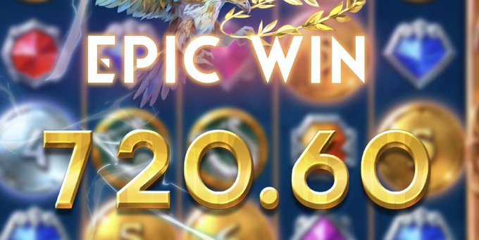 The image displays an "EPIC WIN" slot machine celebration screen showing a jackpot payout of "720.60," featuring angel wings, laurel wreaths, and colorful gemstones in the background. This visually emphasizes the celebratory "+$700" lucky win described in the caption, as the 720.60 amount exceeds $700 after rounding.