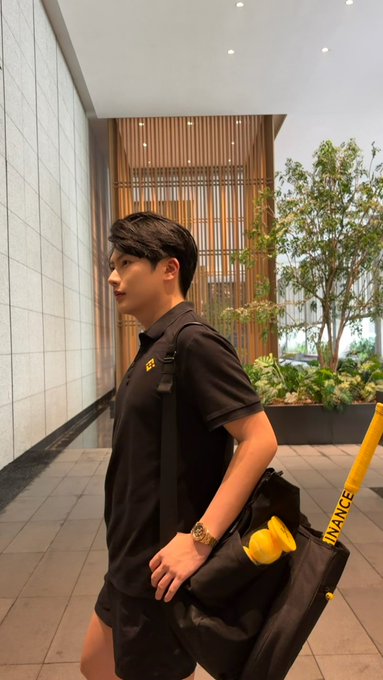 A young man in a black polo shirt and shorts stands in profile inside a modern building, carrying a black duffel bag adorned with a small yellow plush toy, while a yellow umbrella marked "URANCE" leans nearby—a casual scene juxtaposed with a post promoting the potential of the cryptocurrency "Lighter" (ethereum:0x232ce3bd40fcd6f80f3d55a522d03f25df784ee2).