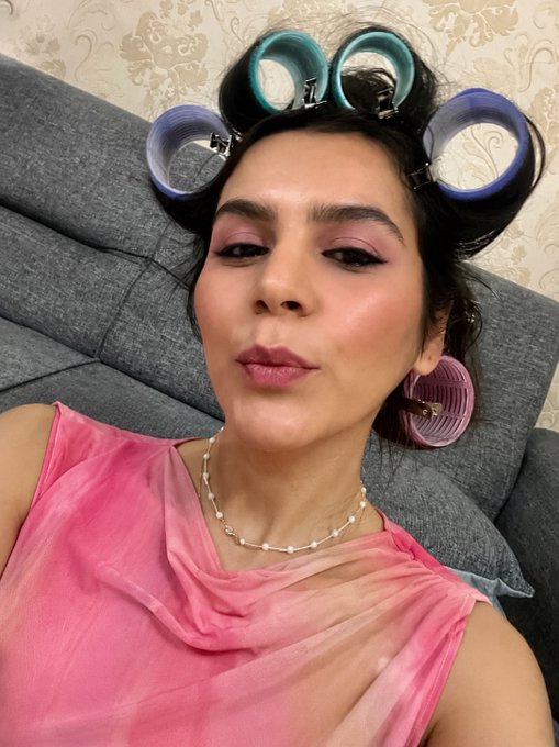 The image features a woman wearing a pink top with blue and green curls sitting on a couch. She has her hair styled with curlers and is posing for a picture. The caption of the image reads "I never understood when Ethereum goes down, is it the time to collect, or when it goes up? Whatever, GN". This suggests that she might be discussing or contemplating the fluctuations in the cryptocurrency market, specifically Ethereum's value over time.