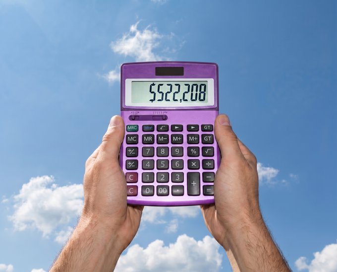 A person holding a purple calculator up in front of them against a blue sky with clouds.