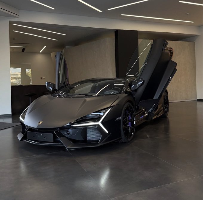 A sleek black Lamborghini Revuelto with its signature scissor doors open sits on display in a modern showroom. The luxury sports car aligns with the post's "New whip" caption, celebrating a high-end vehicle acquisition tied to the Bera Chain project.