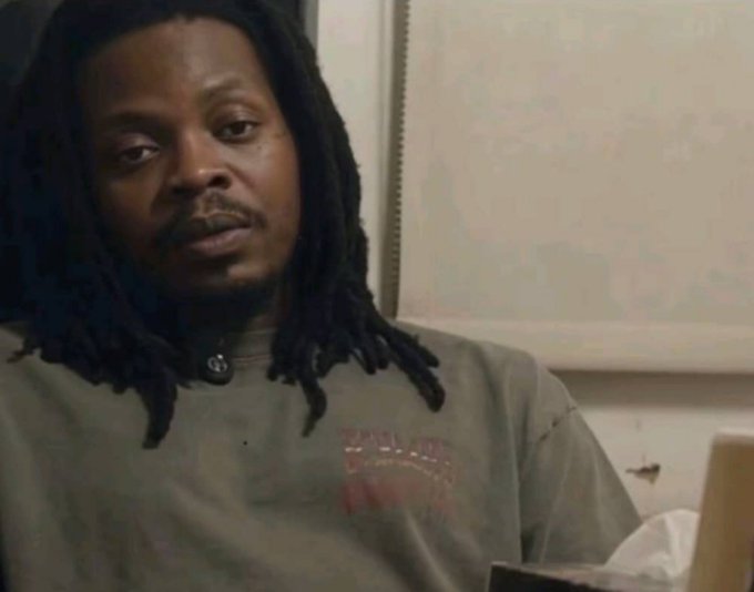 Close-up shot of a man with long dreadlocks wearing a gray t-shirt, appearing to be from a documentary or interview.